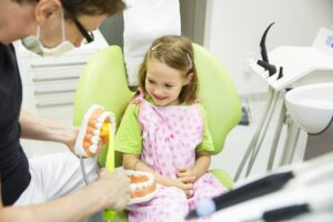 Pediatric dentist educating a smiling little gir