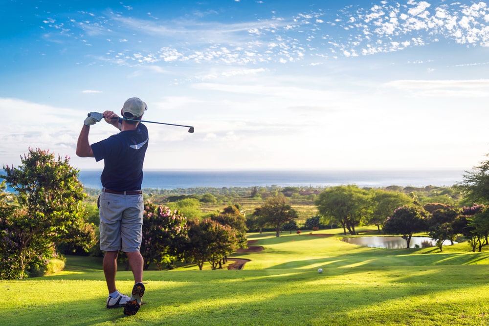 Man hitting golf ball down hill towards ocean