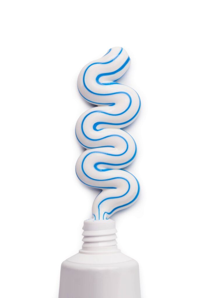toothpaste container with squeezed out striped toothpaste on white background