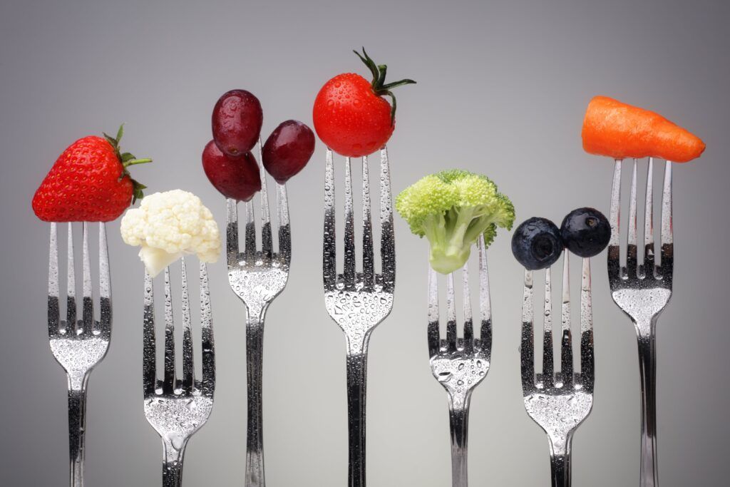 strawberry, cauliflower, grapes, tomato, broccoli, blueberry, and carrot stick shown on different forks
