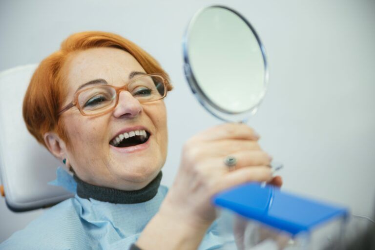 senior woman looking in mirror sitting in dental chair