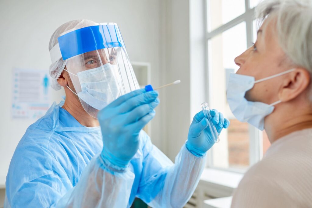 Professional medical worker wearing personal protective equipment testing senior woman for dangerous disease using test stick