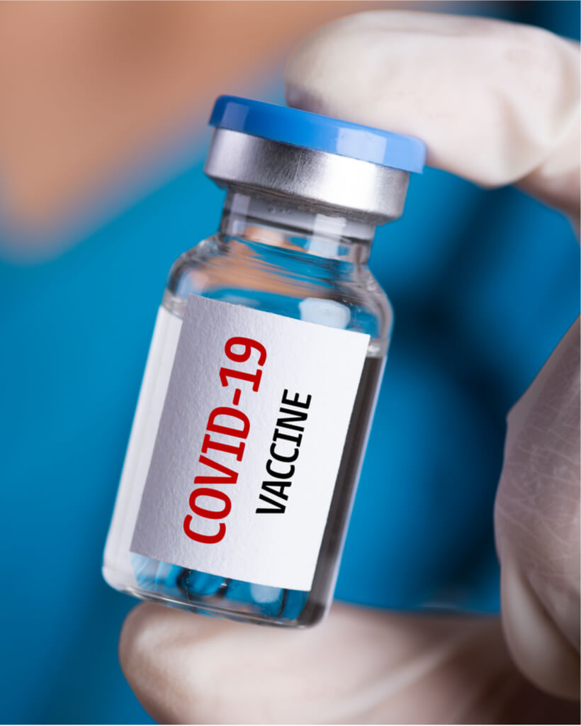 Female doctor with a stethoscope on shoulder holding syringe and COVID-19 vaccine