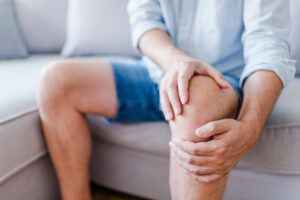 Man suffering from knee pain sitting sofa.