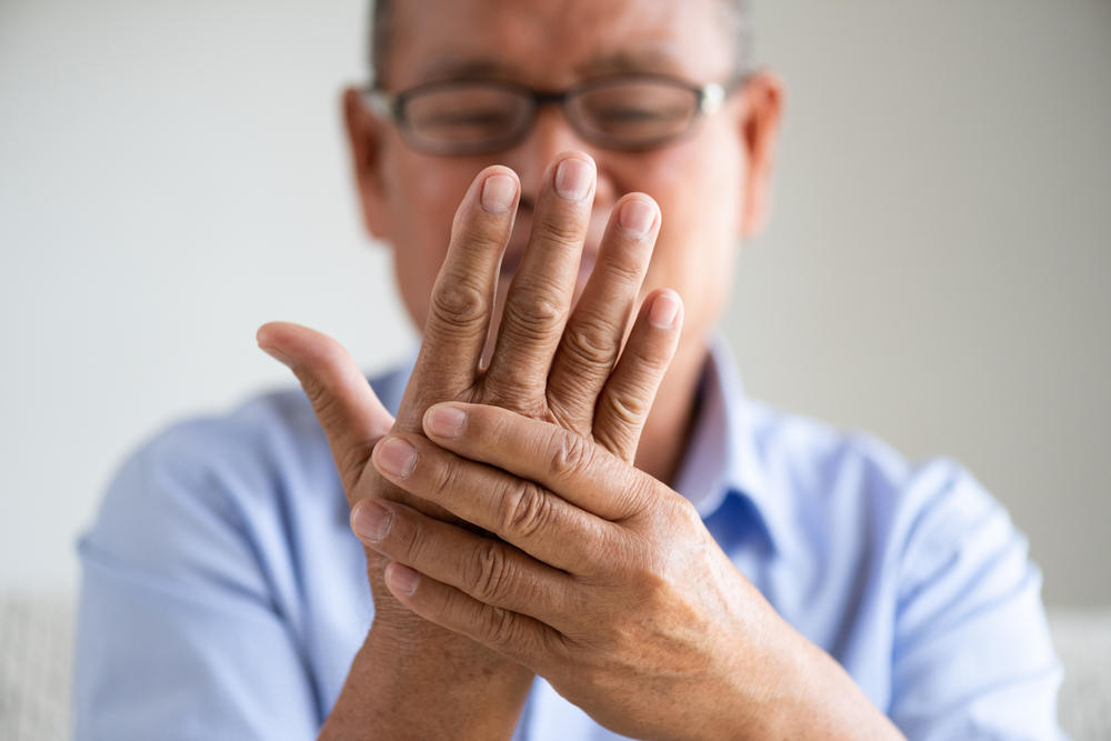 Asian old man sitting on sofa and having hand pain, hand injury at home.