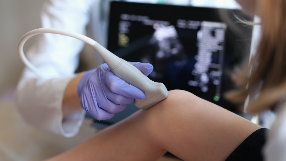 Doctor conducting ultrasound examination of knee joint in child closeup.