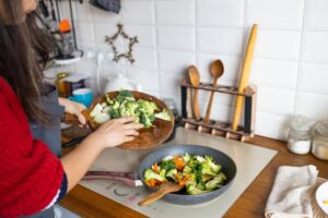 Woman cooking frying fresh healthy vegetables on pan on induction stove. Lifestyle background.