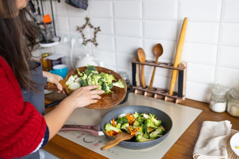 Woman cooking frying fresh healthy vegetables on pan on induction stove. Lifestyle background.