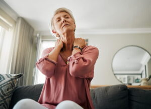 Senior woman, neck pain and stress in living room home of spine injury, fibromyalgia and osteoporosis