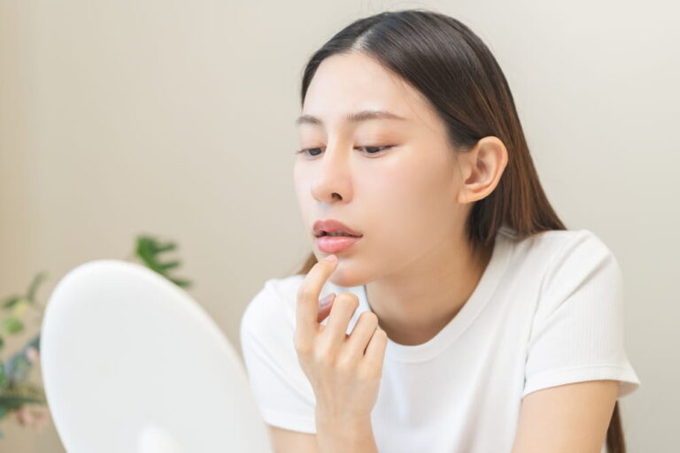 young woman finger touching lips in front of mirror after applying lipstick balm on dry mouth
