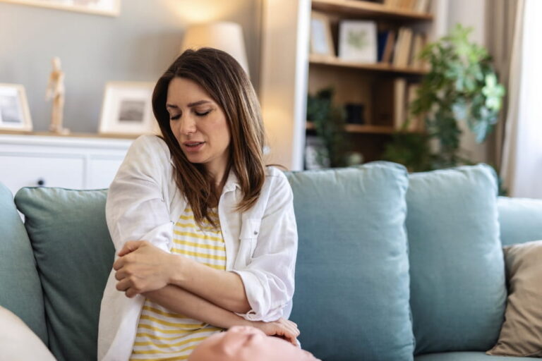 Elbow, injury and hand of woman on a sofa with problem, arthritis or osteoporosis in her home.