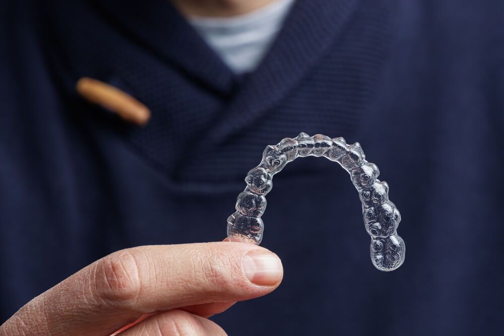 Man holding one transparent aligner. Invisalign orthodontics concept