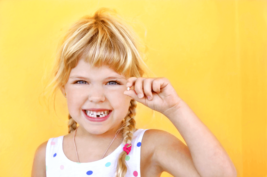 Smiling girl holding missing tooth