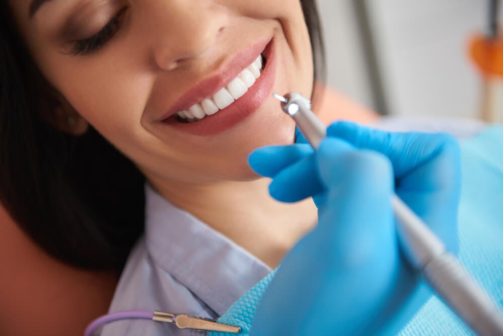 Dentist in sterile gloves doing professional teeth cleaning for smiling lady