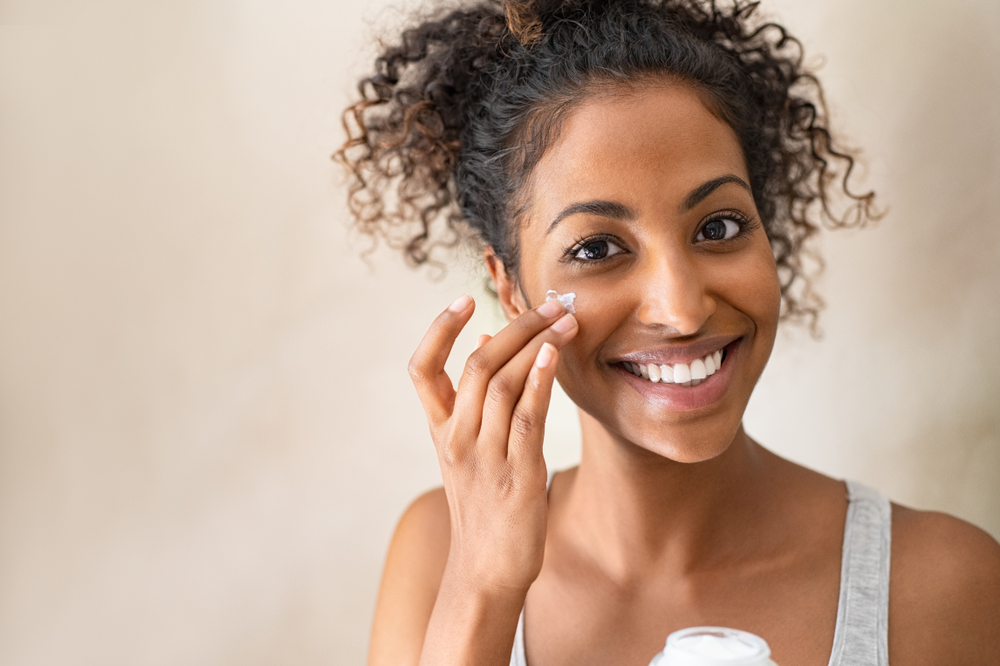 Smiling girl with applying facial moisturizer