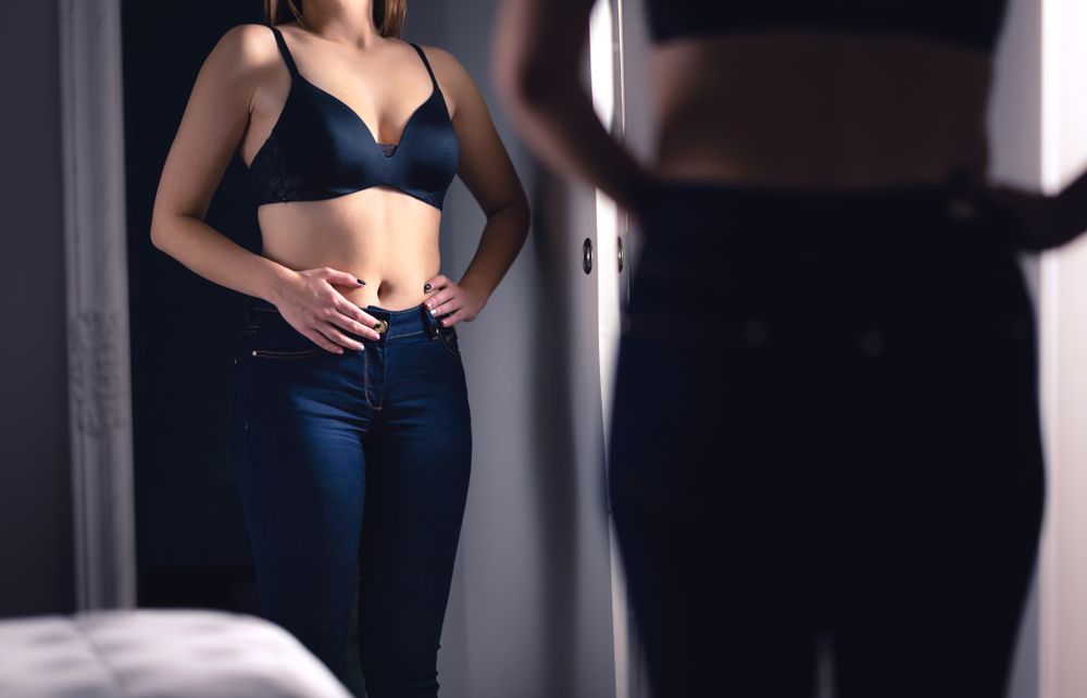 Woman looking in the mirror debating if she wants to get a Tummy Tuck