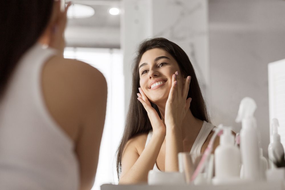 Happy woman smiling in the mirror after visiting a doctor for Neurotoxins