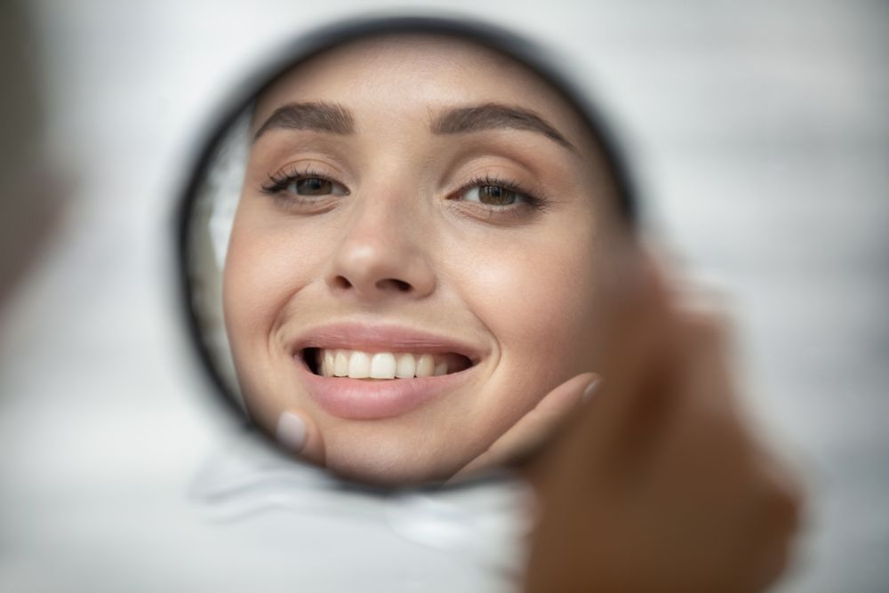 Woman smiling in a small mirror after getting Fillers