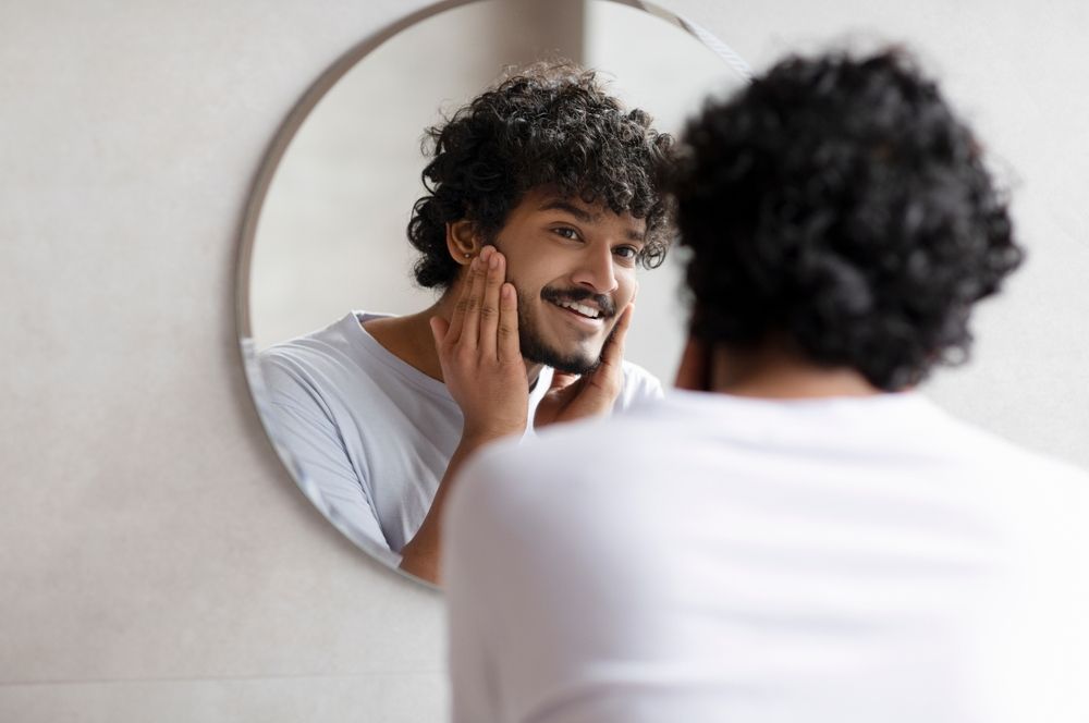 Man smiling in the mirror after using Skin Care products