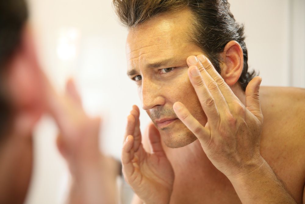 Man looking in the mirror thinking about getting Laser Treatments for his skin