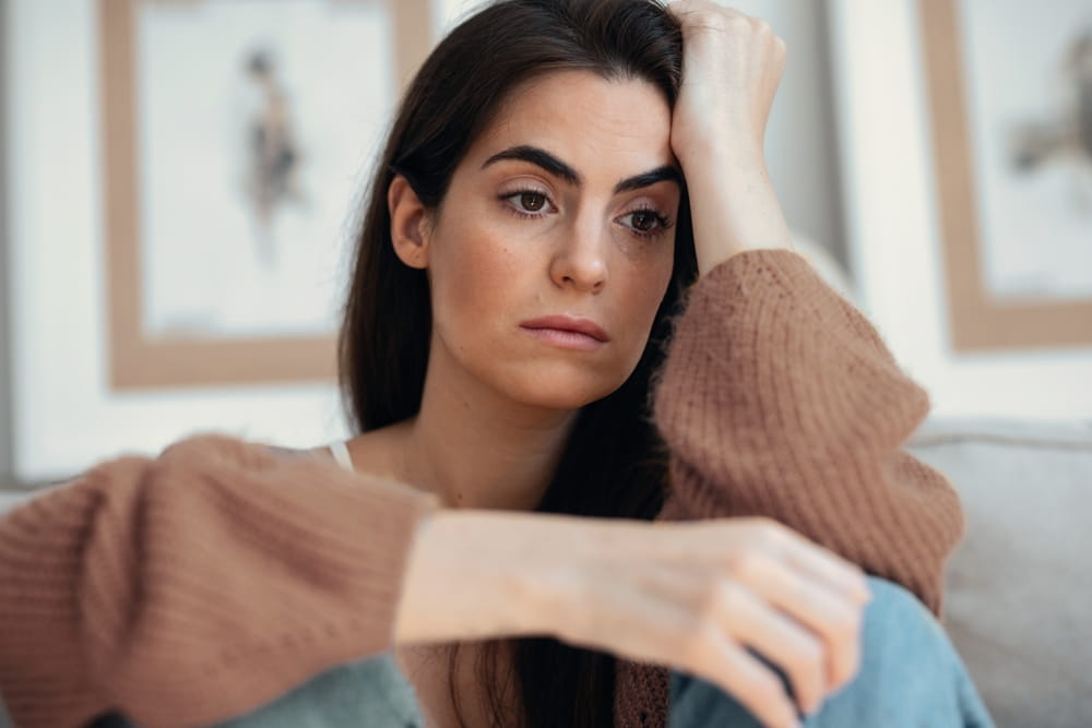 Shot of depressed young woman overthinking while sitting on the couch at home
