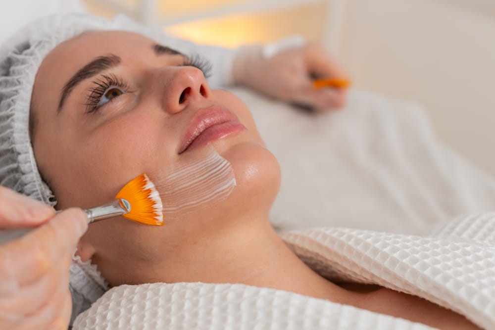 Enzyme therapy. Beautician applying moisturizing medical chemical peeling cream mask on young adult woman face