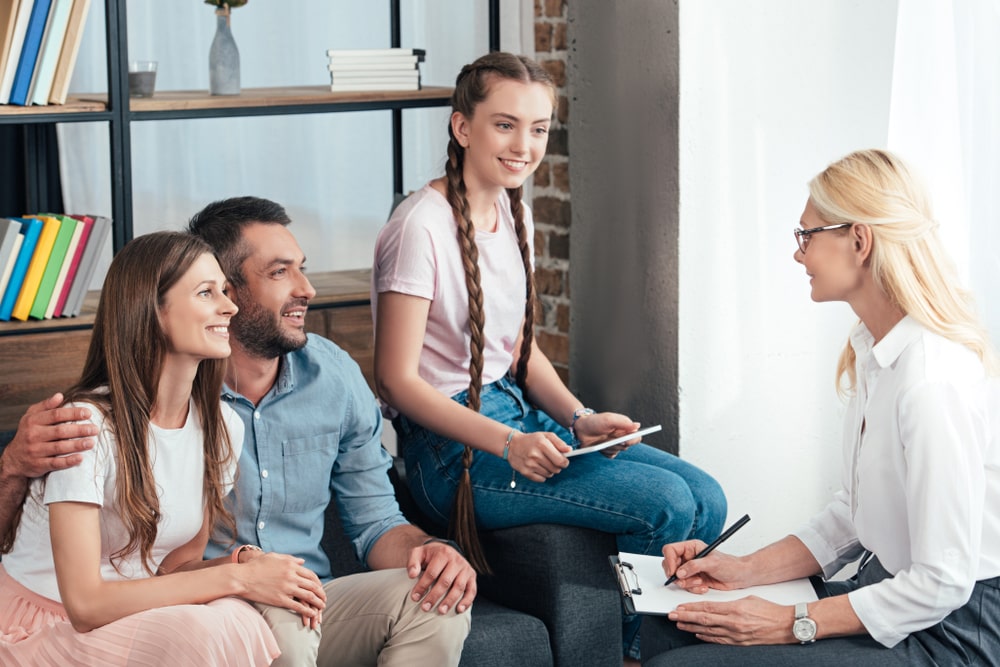 female counselor writing in clipboard on therapy session of family