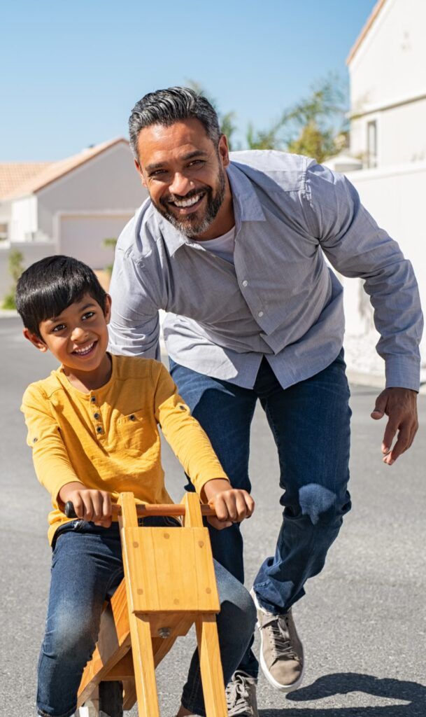 Happy father helping smiling boy to ride wooden cycle