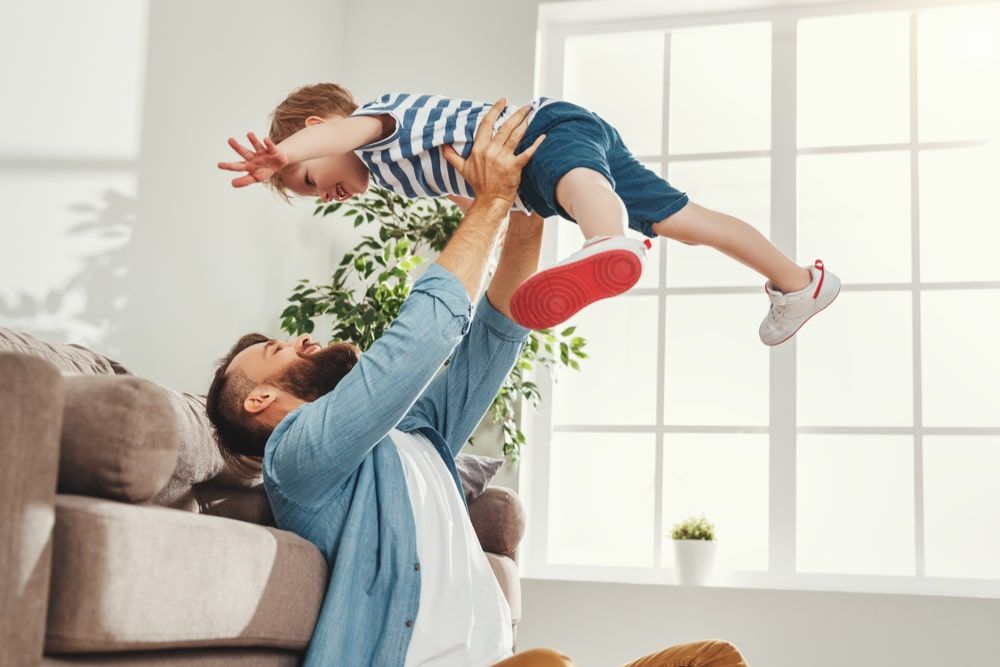 Man sitting on floor and throws up happy little son