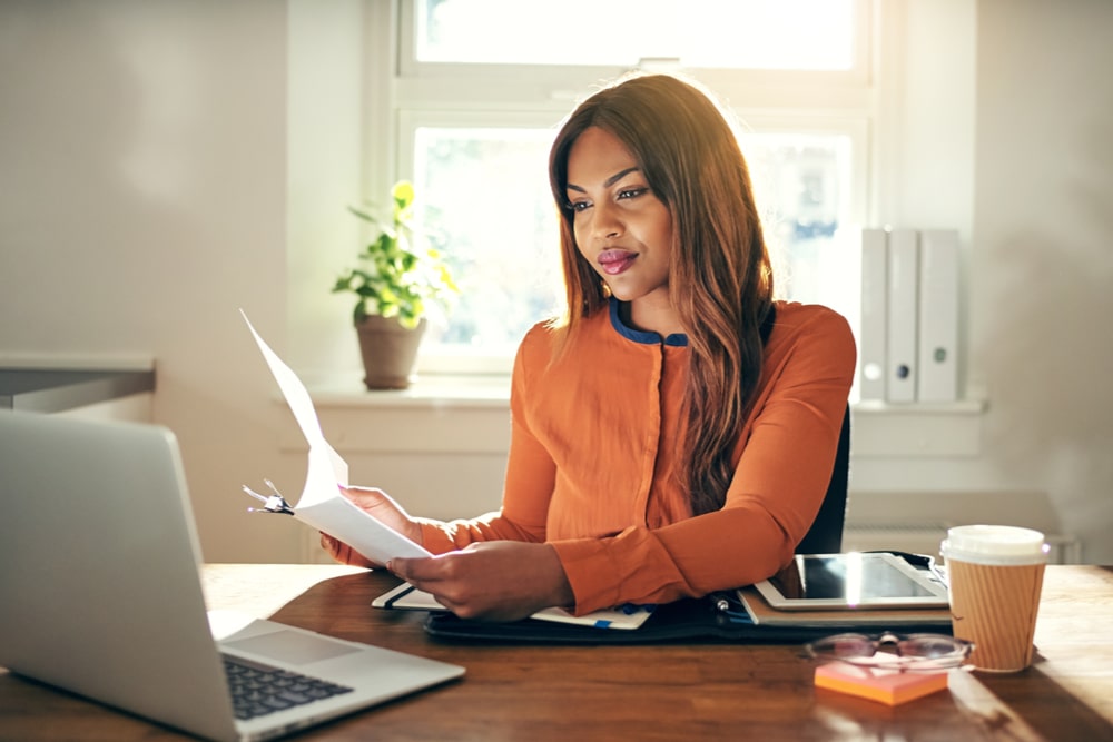 Smiling female sitting at a table in her home office reading paperwork