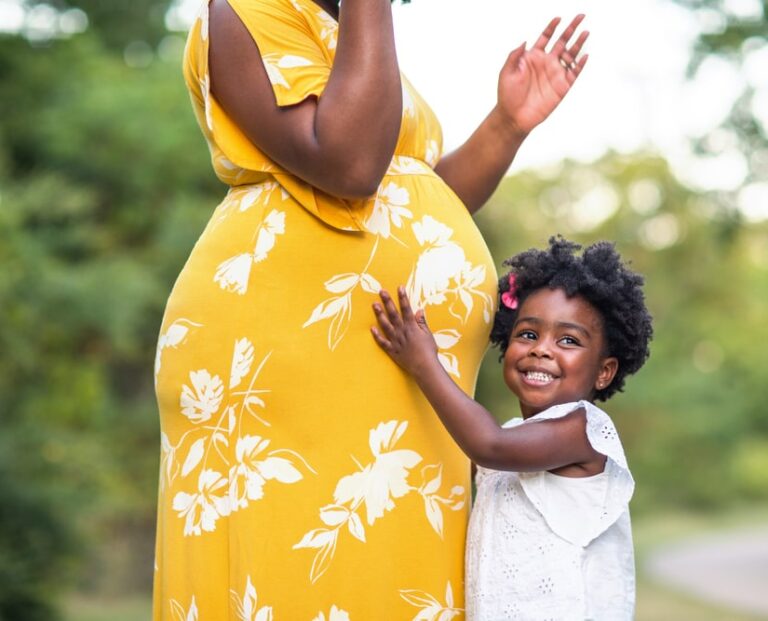 Little girl smiling holding her mother’s stomach who is pregnant