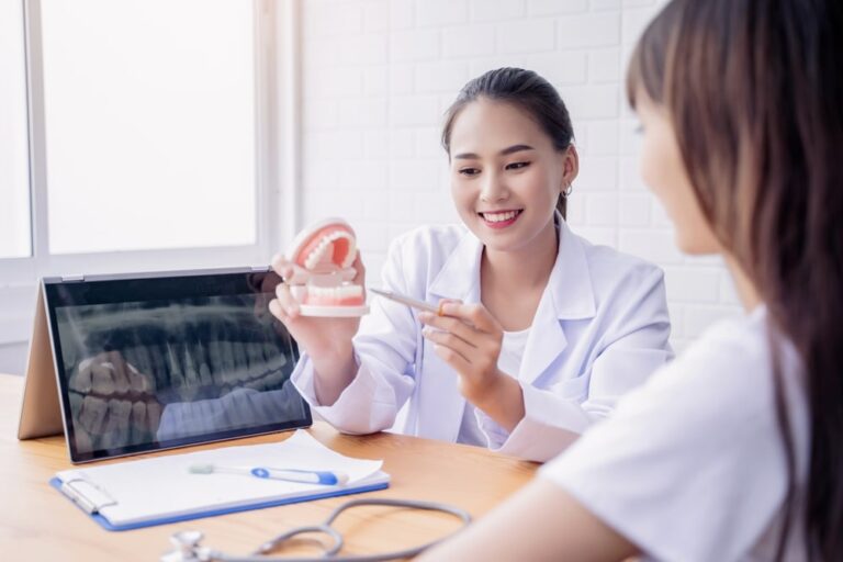 Happy smiling Asian female dentist doctor examining teeth model