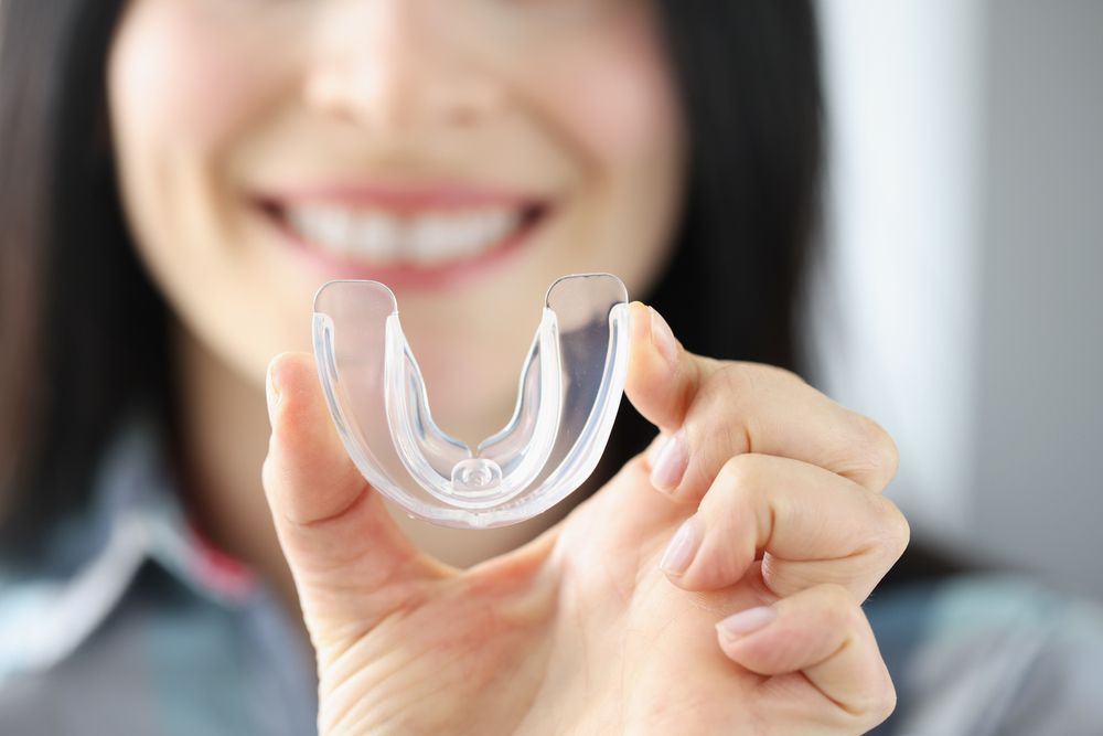 Person smiling holding up a mouth guard after seeing the benefit of Oral Appliances