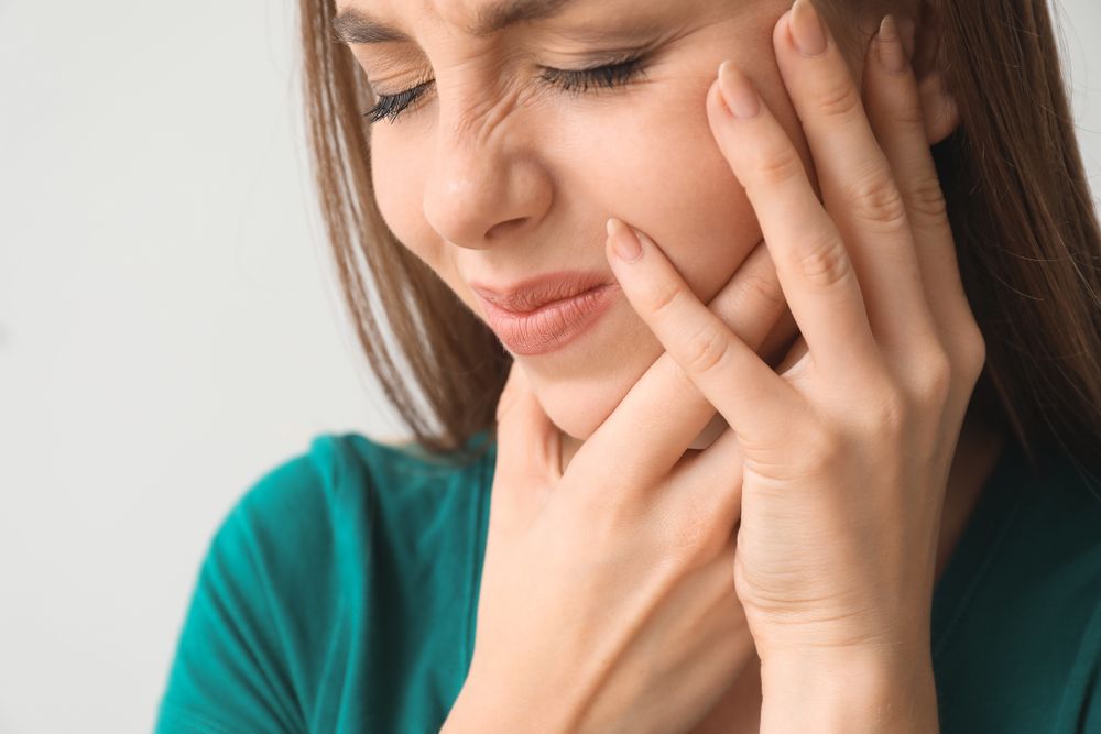 A woman holding her jaw whose experiencing dental emergencies 