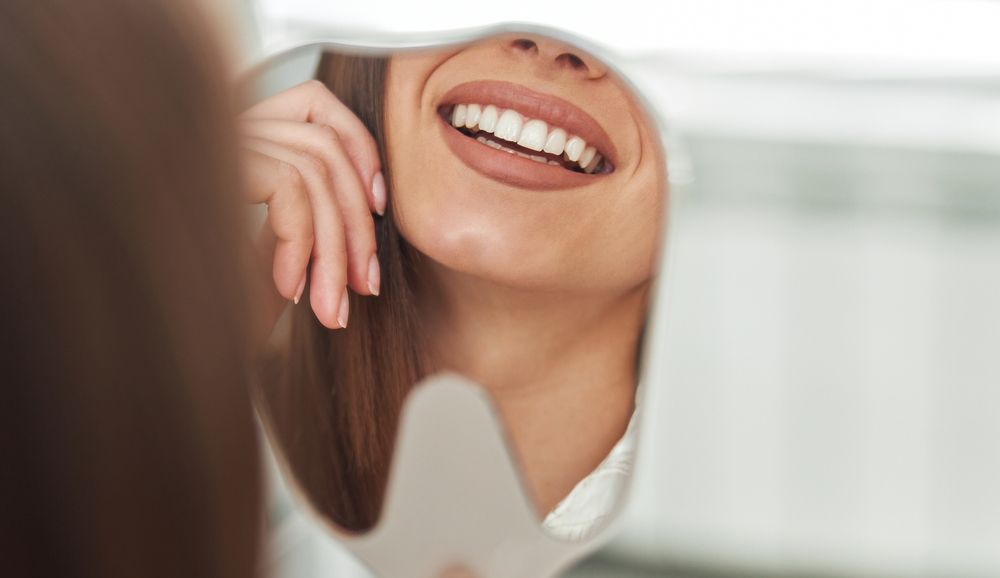 A woman smiling in the mirror after receiving Restorative Dentistry