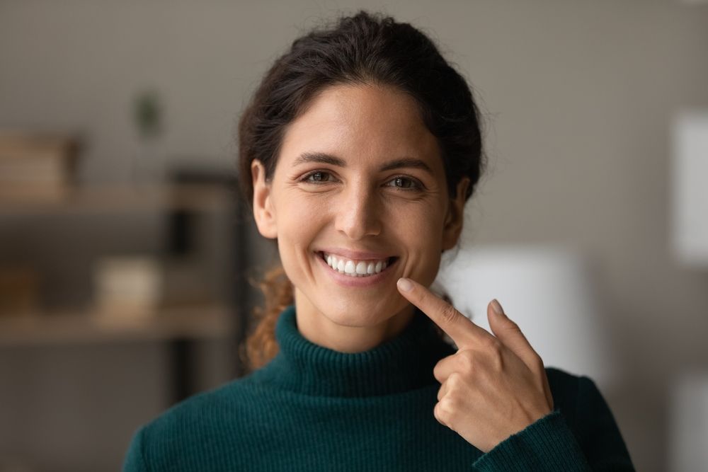 Woman pointing at her smile after getting Porcelain Veneers 