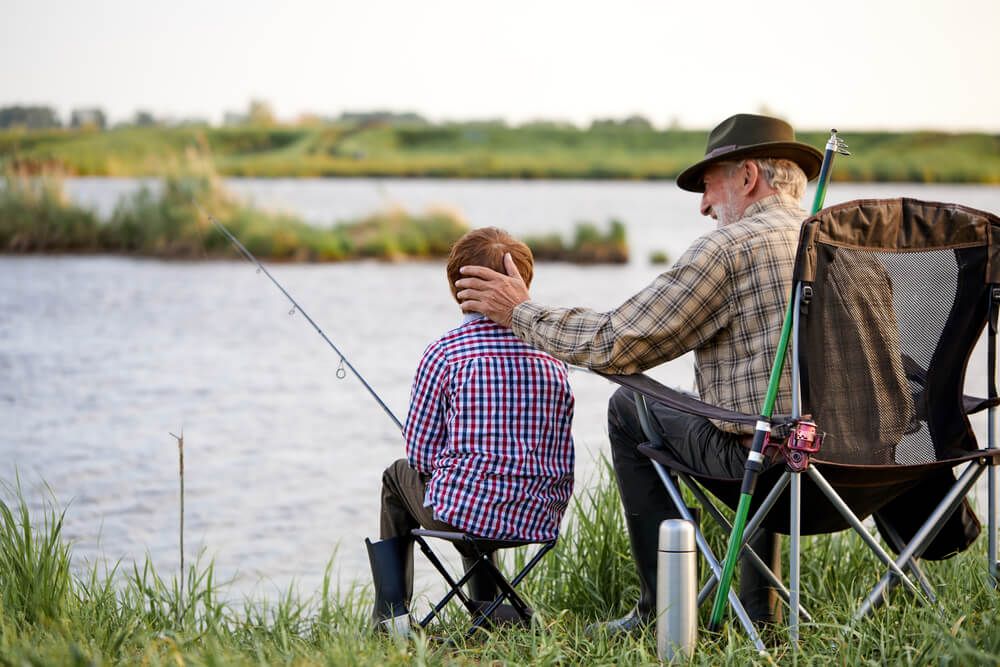 loving grandfather and boy fishing by lake together during camping trip in nature,