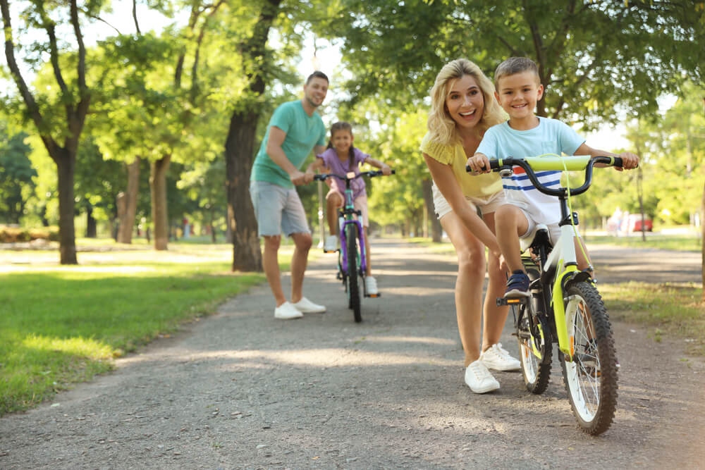 Happy parents teaching their children to ride bicycle in park