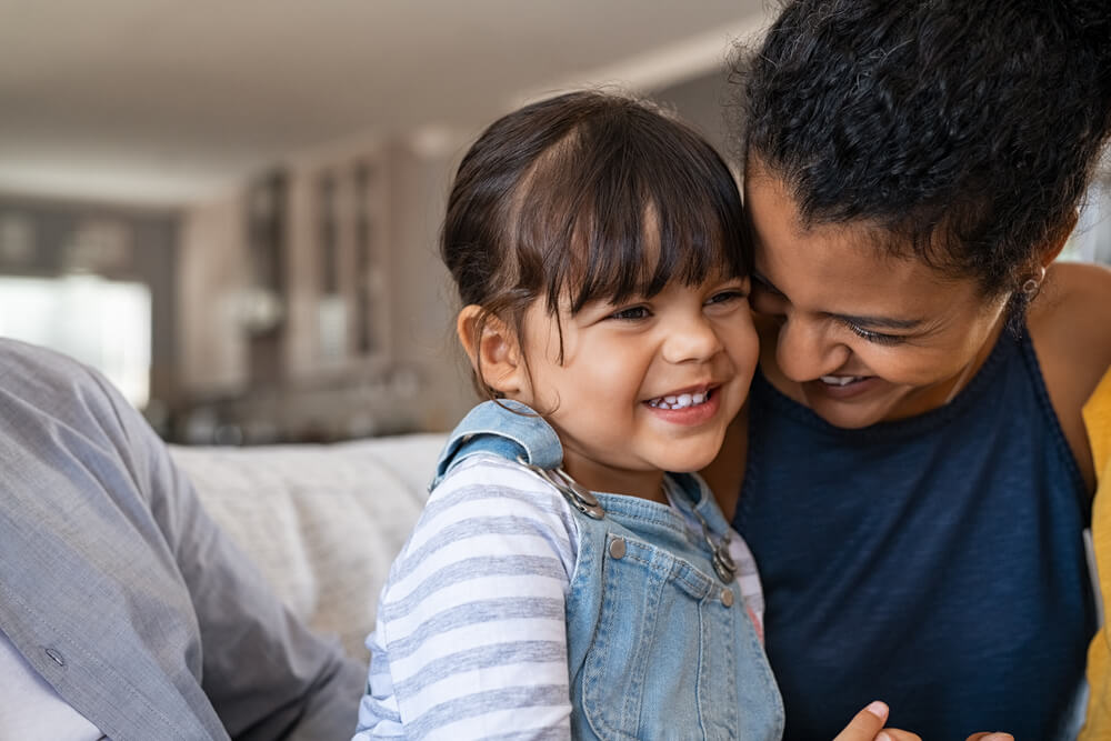 Beautiful black mother embracing little girl sitting on couch with copy space