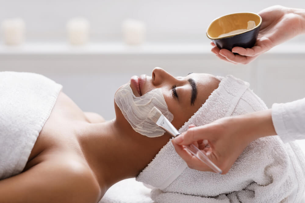 Beautician Applying Clay Face Mask On Black Woman Face