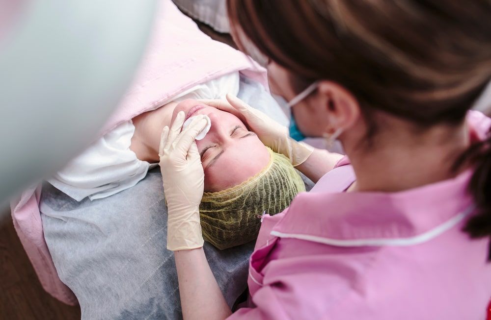 cosmetologist prepares the skin of the patient's face for chemical peeling