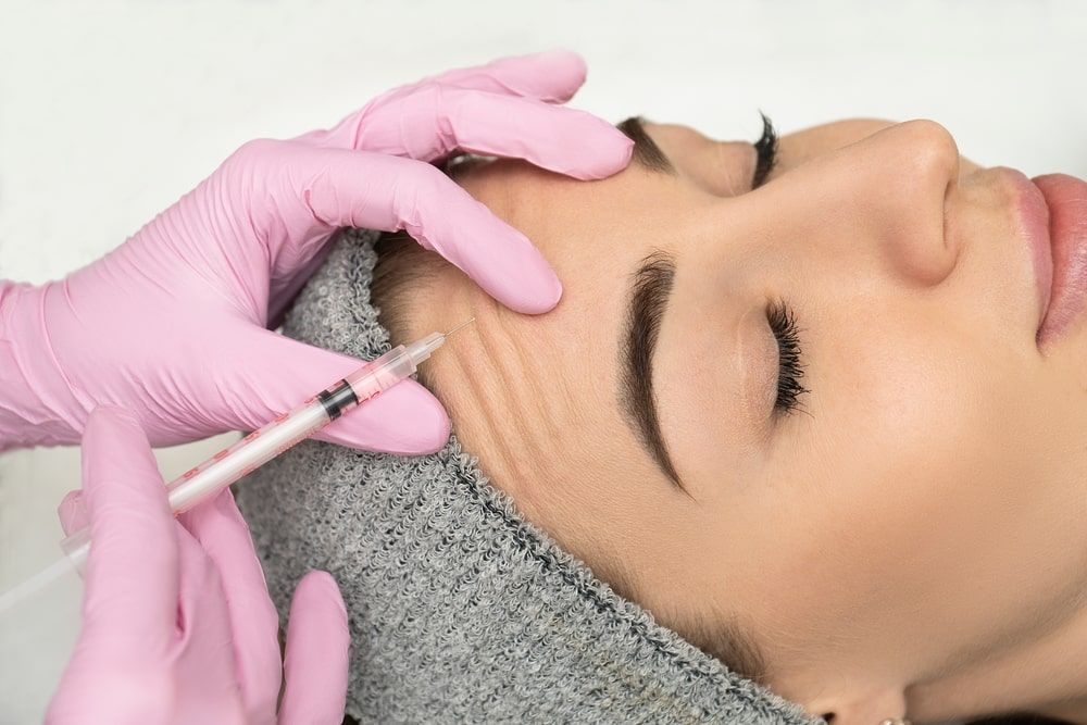 expert cosmetologist injecting botox into a woman's forehead