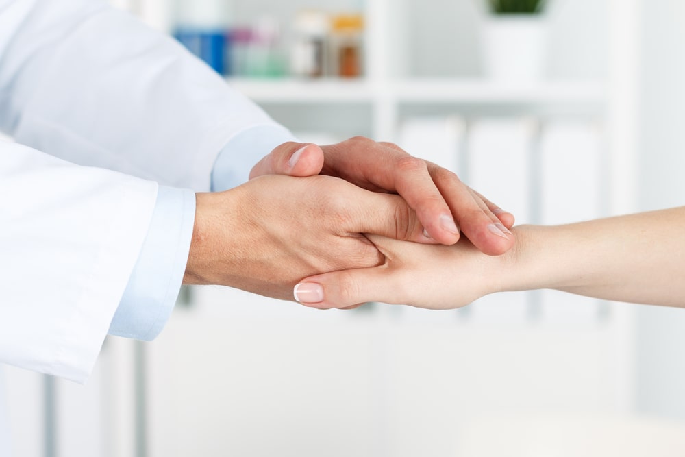 Friendly male doctor's hands holding female patient's hand for encouragement and empathy