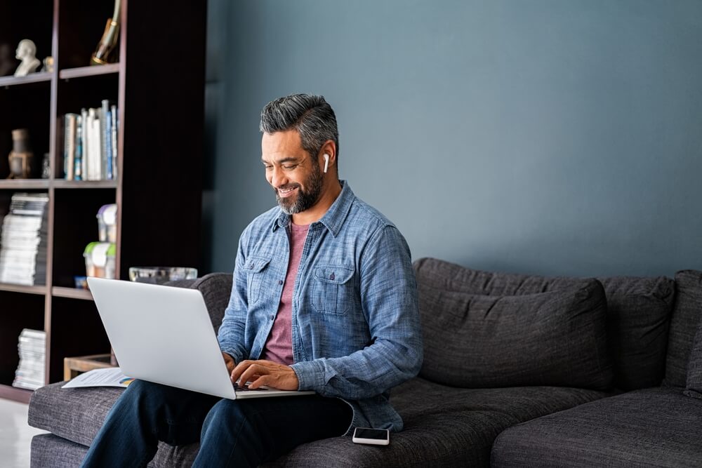 Successful mature indian businessman sitting on couch typing on laptop