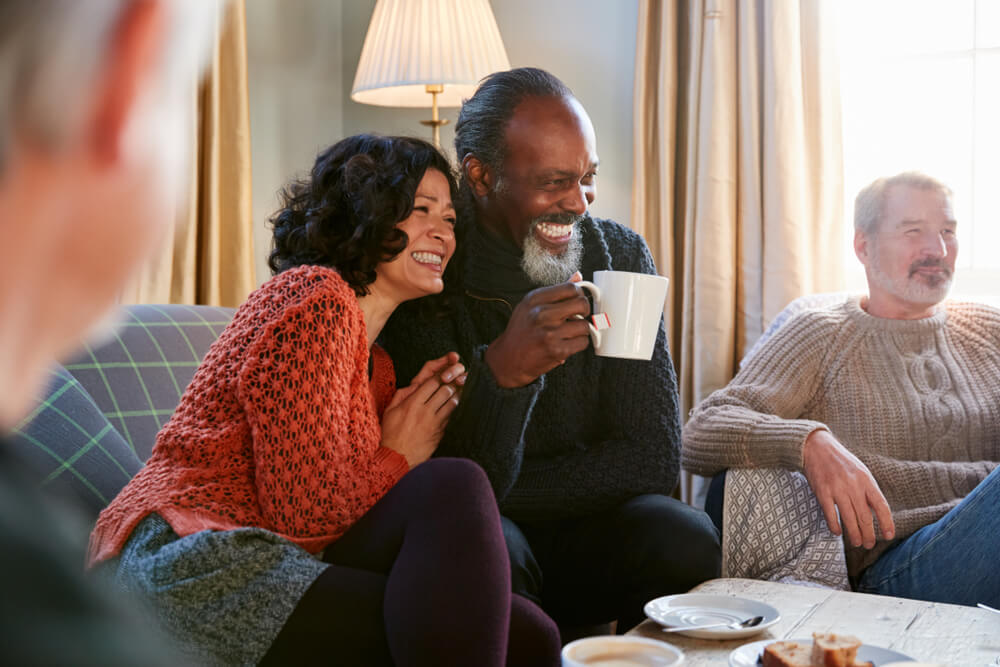 Middle Aged Couple Meeting Friends Around Table In Coffee Shop