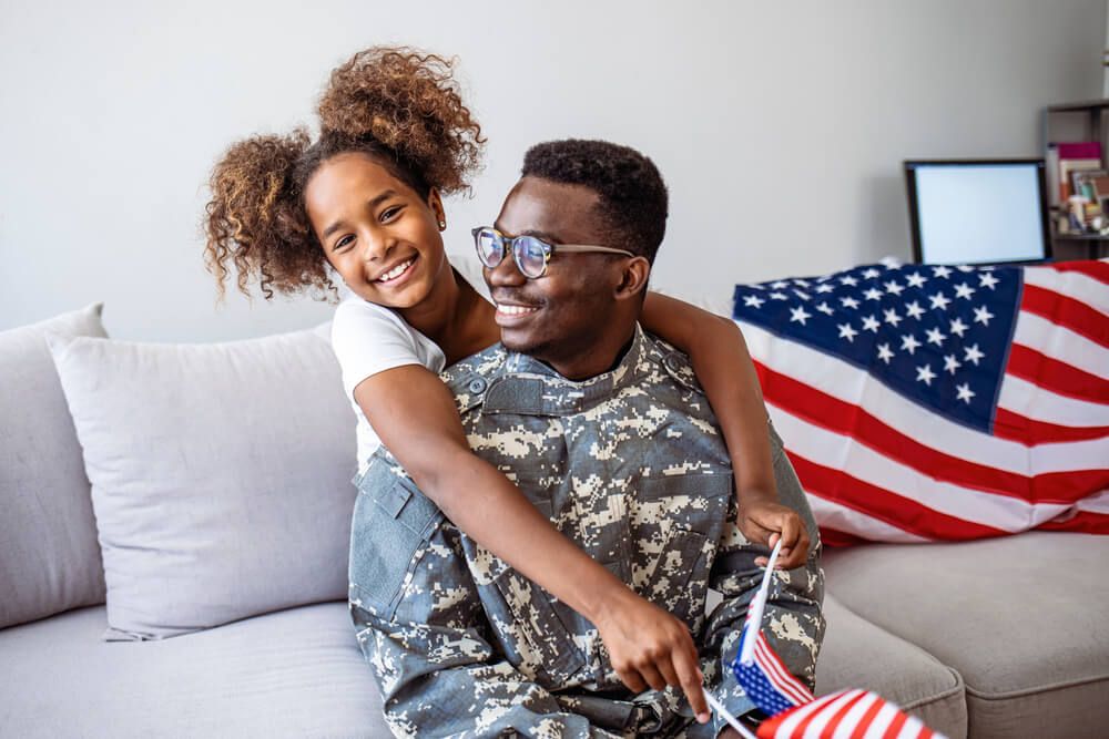 Happy little girl daughter with American flag hugging father in military uniform
