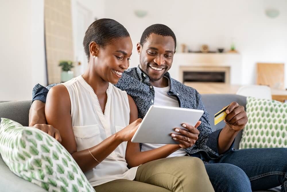 Black wife doing shopping online while using digital tablet at home with husband