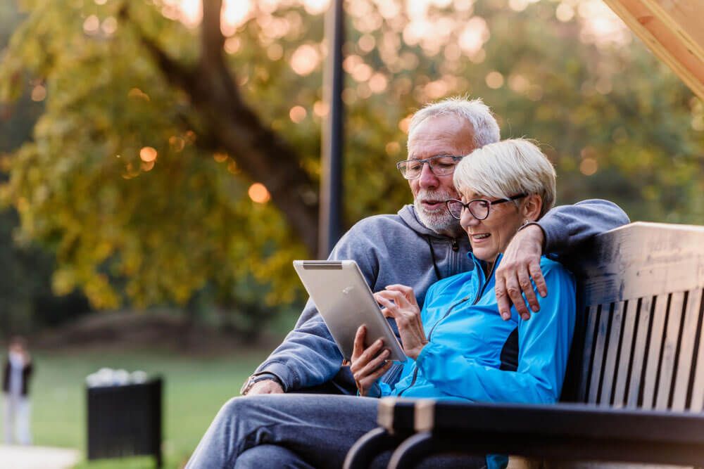 Smiling senior active couple sitting on the bench looking at tablet computer