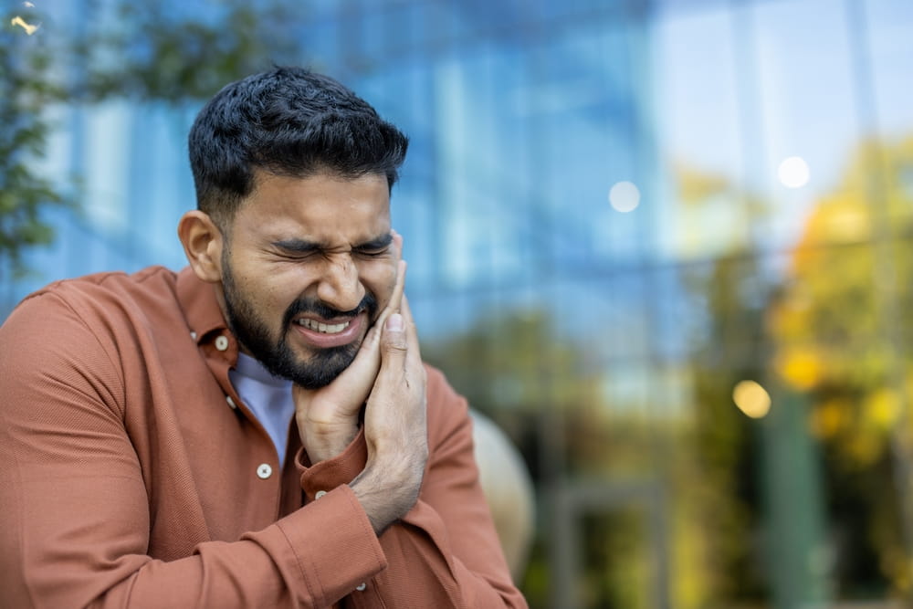 An indian man is experiencing a severe toothache, he is holding his face in pain and discomfort.