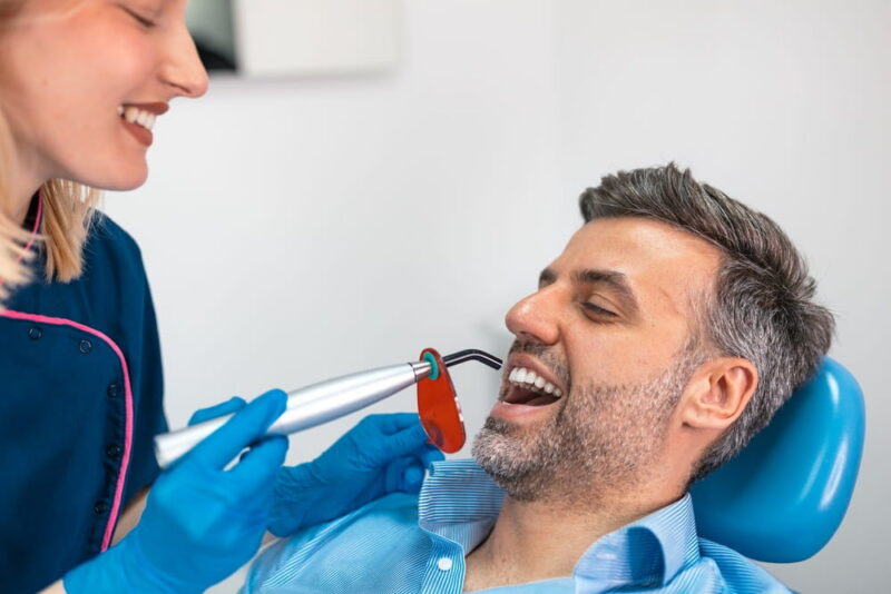 Dental curing light treatment. Professional female dentist using UV lamp to harden filling on a male patient in clinic,